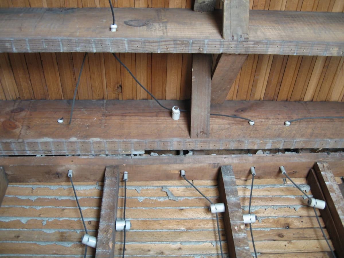 Knob-and-tube wiring in a 1930 house: single cloth-covered conductors run between wooden joists, held off the wood by white porcelain knobs and passed through porcelain tubes