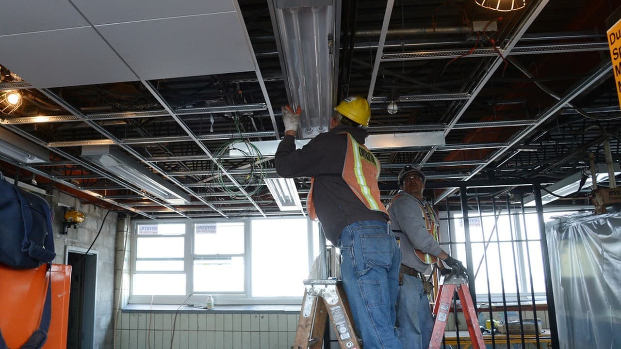 Two electricians install overhead systems inside a commercial building.