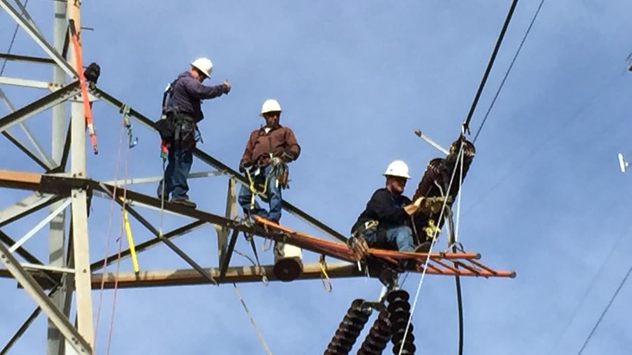 A line crew in protective equipment works together on electrical infrastructure.