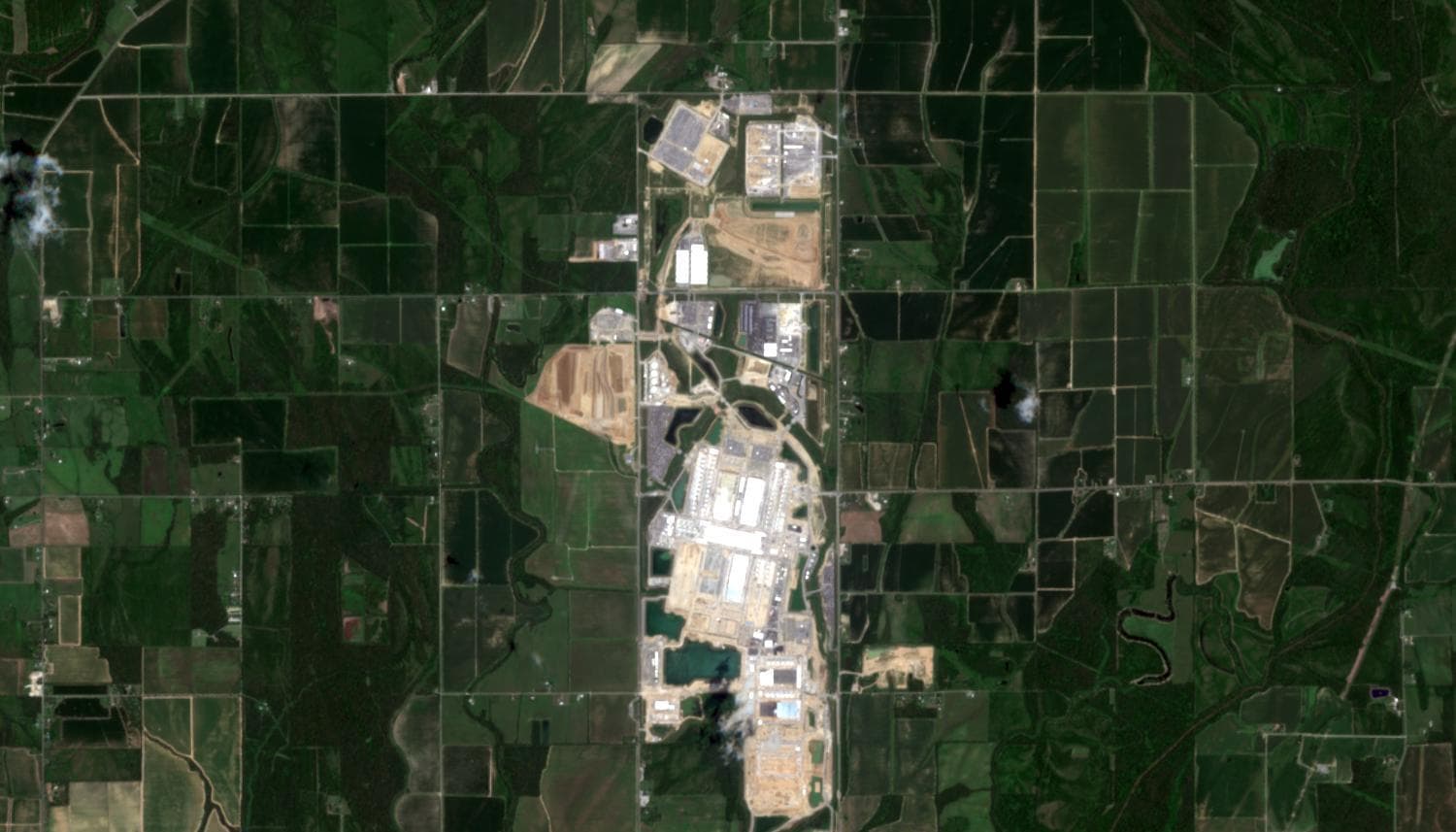 Satellite view of Meta's Hyperion data-center construction site in Richland Parish, Louisiana: a long corridor of white building slabs, cleared tan earth, and cooling ponds surrounded by green farmland.