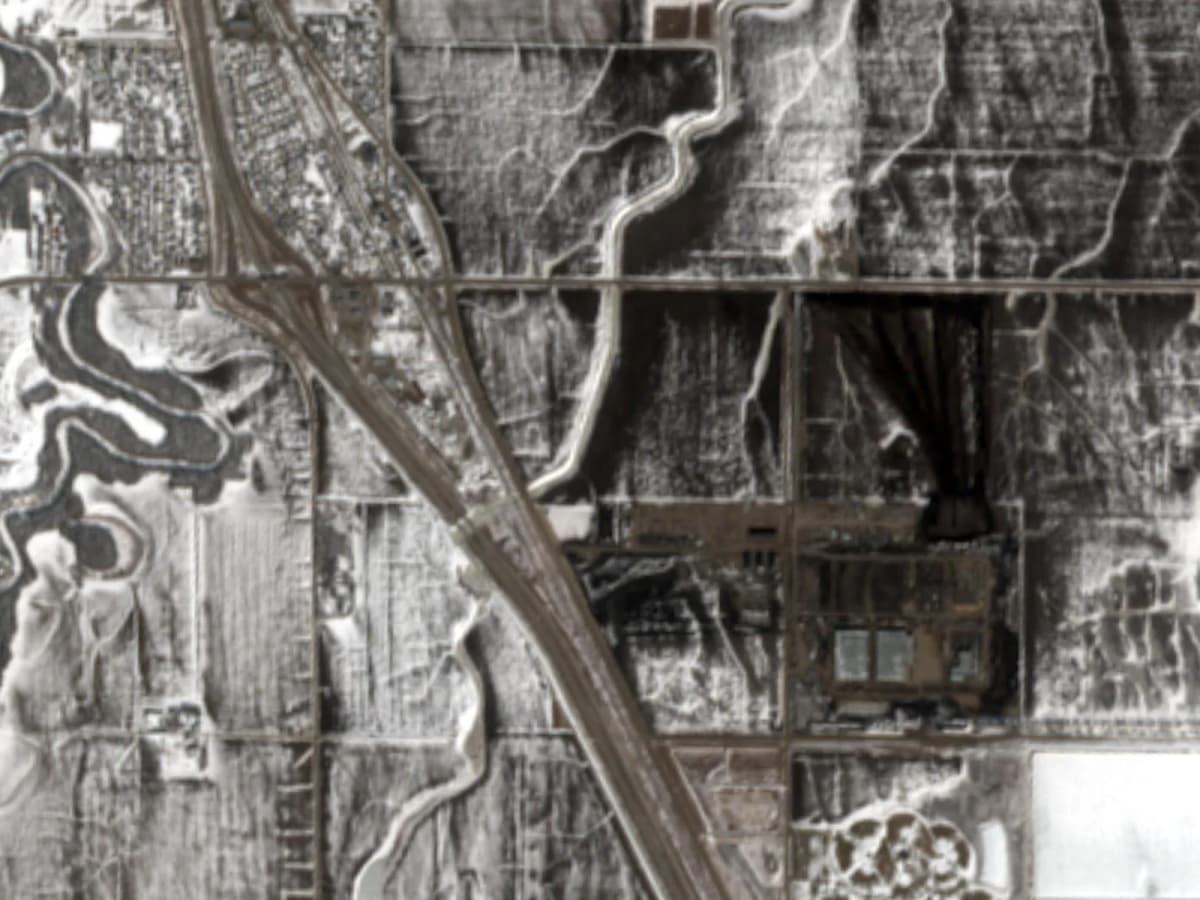 Satellite view of the Polaris Forge 2 construction site in March 2026: the graded campus is a dark rectangle against snow-covered farmland, with Interstate 29 and the town of Harwood to the upper left