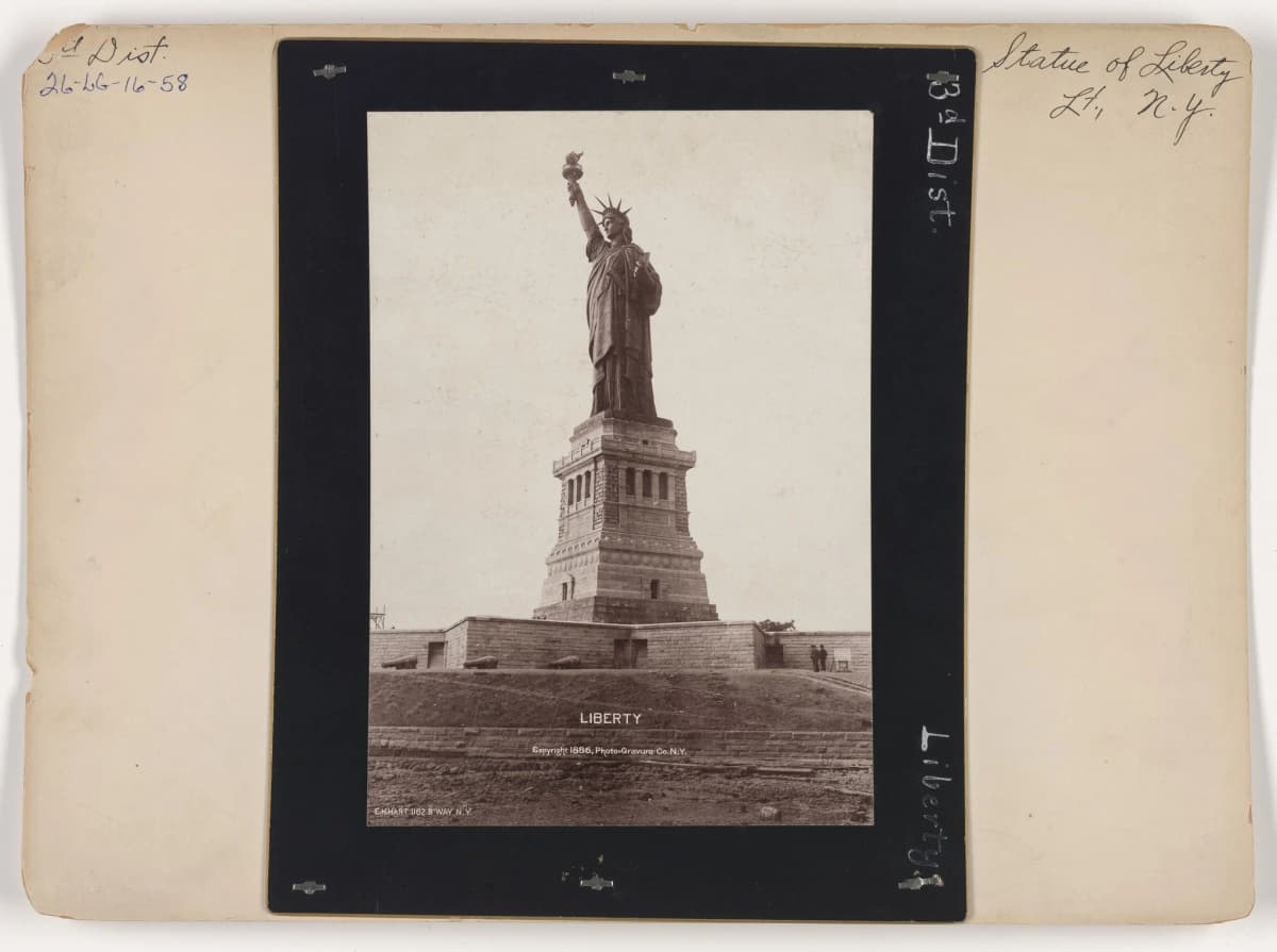 Sepia 1886 photograph of the Statue of Liberty and its torch on the pedestal above Fort Wood, mounted on a lighthouse-records card handwritten Statue of Liberty Lt., N.Y. and 3d Dist.